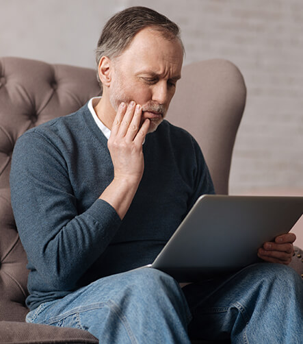 man holding his jaw in pain while looking at his laptop