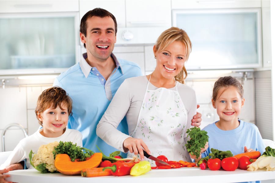 Family of four in the kitchen with healthy food choices before them on the counter.