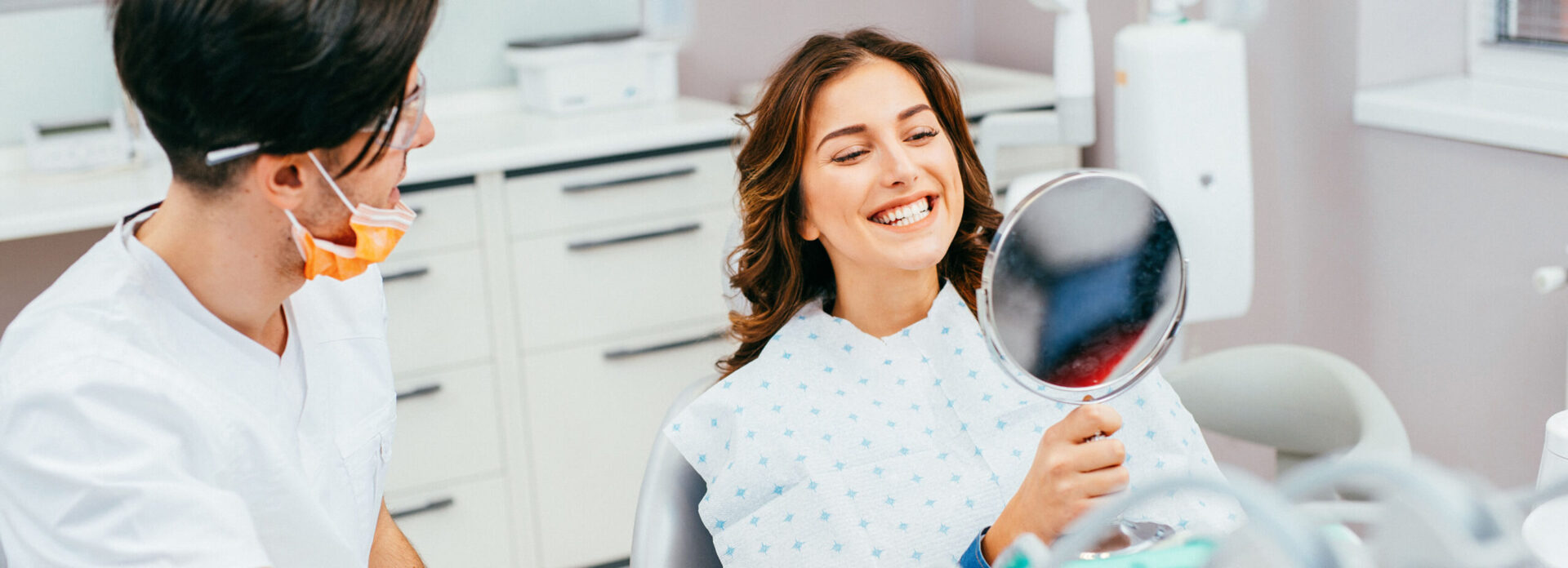 woman examining her bright, white smile in a mirror at the dentist's office
