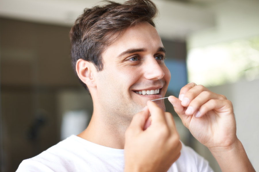 A young adult man flossing his teeth.