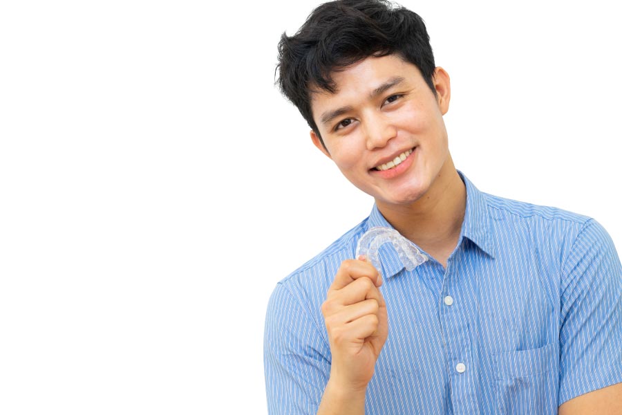 young man holds up his ClearCorrect aligner and smiles showing off his straight teeth