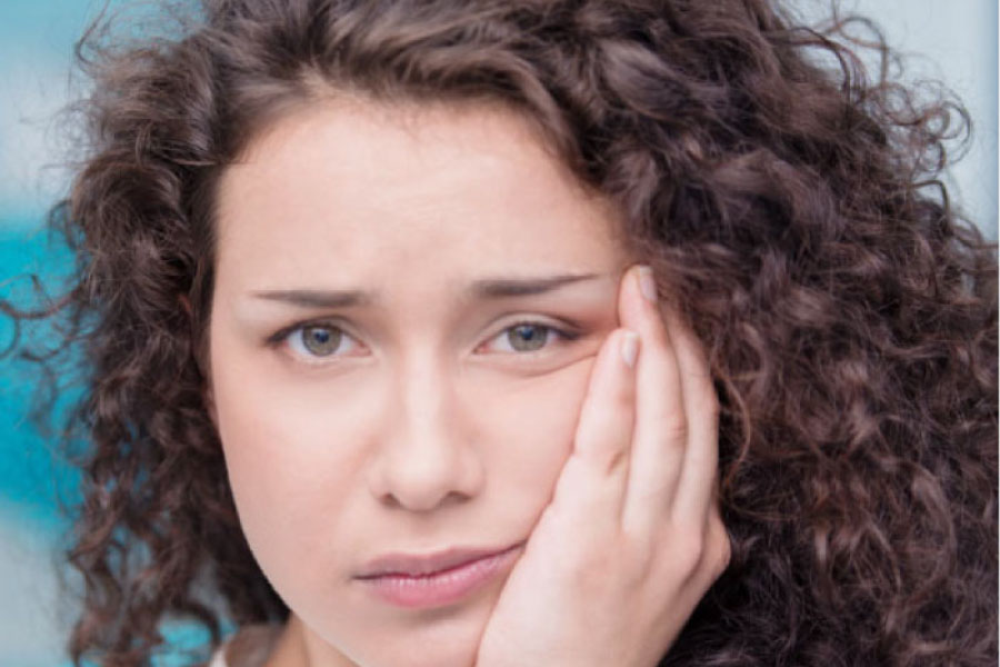 young woman holds her cheek in pain from impacted wisdom teeth